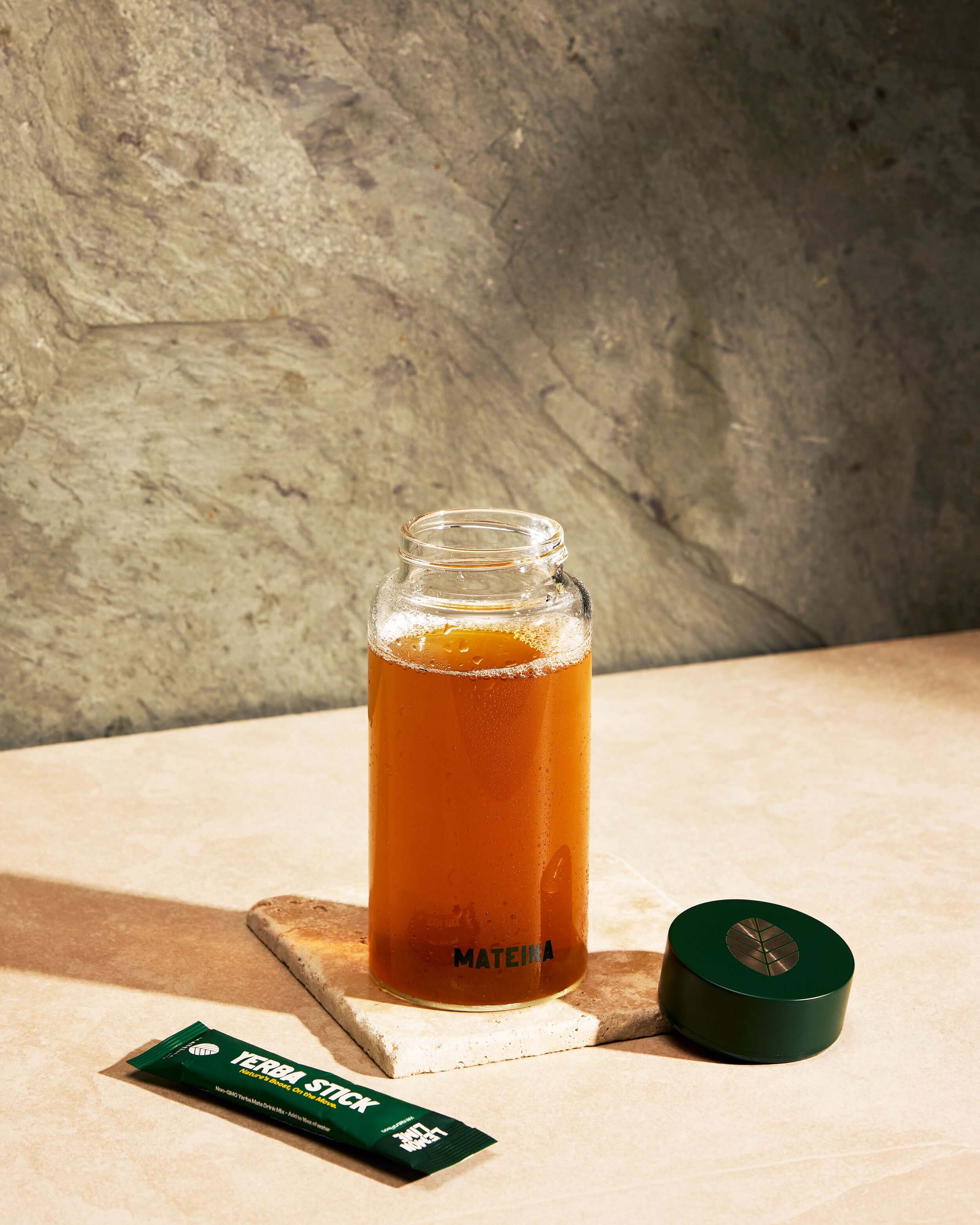 Yerba Mate + Electrolytes - Lemon Lime drink in a jar with a green cap and yerba stick packet on a stone surface.